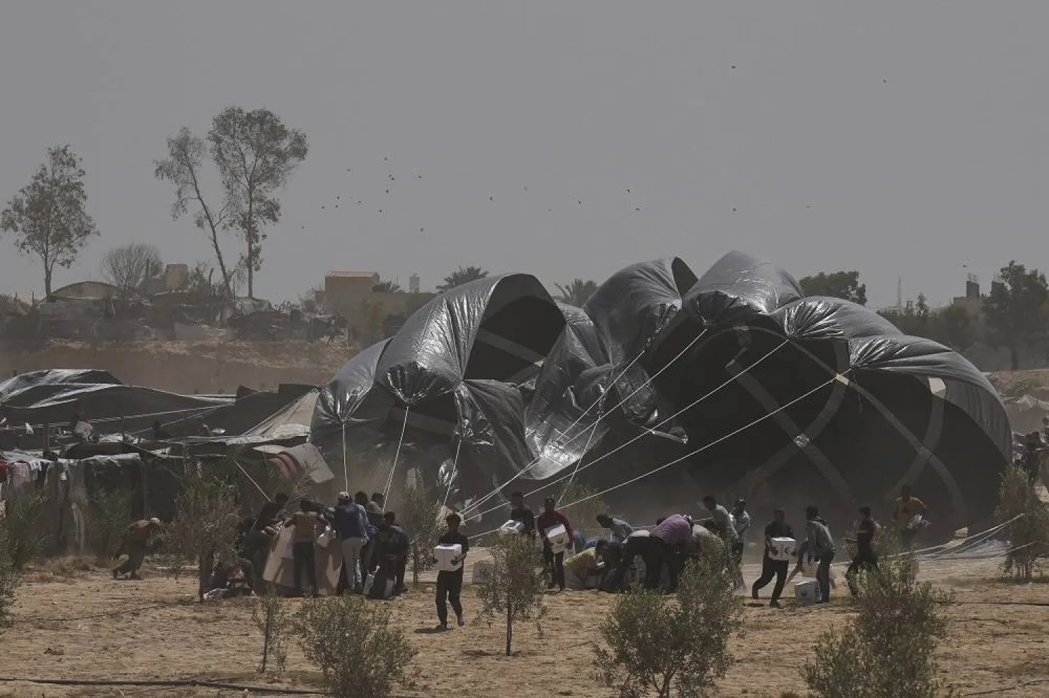 Palestinians rush to collect humanitarian aid packages from the United Arab Emirates, airdropped by parachutes into Deir al-Balah, central Gaza Strip, Tuesday, Aug. 19, 2025. (AP)