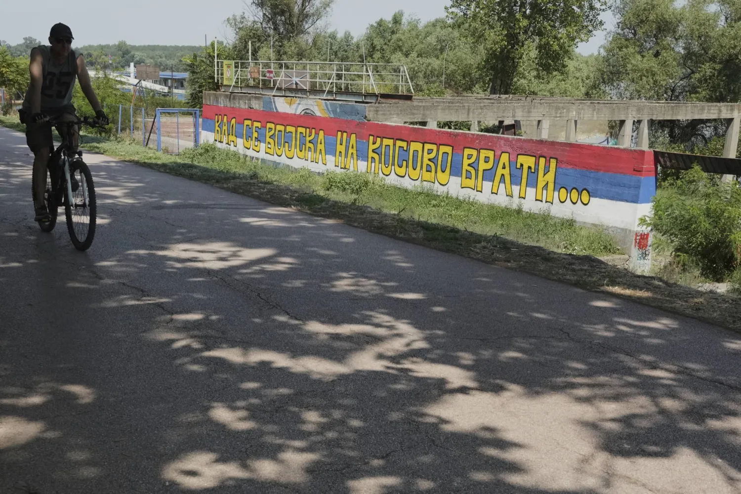 A man rides a bicycle past a mural painted in colors of the Serbian flag, in Belgrade, Monday, Aug. 11, 2025. (AP Photo/Darko Vojinovic)