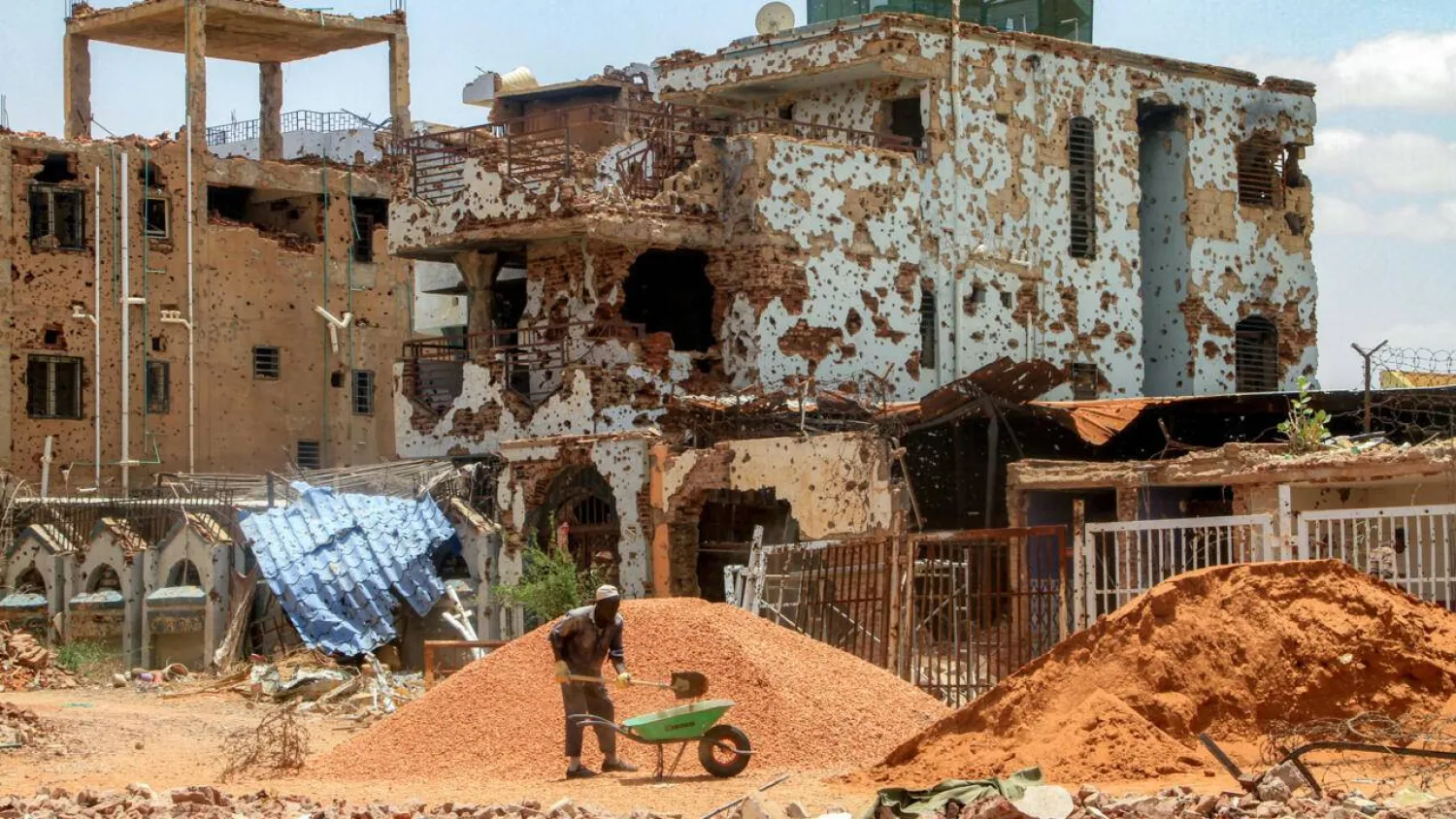 (FILES) A worker shovels pebbles from a mound into a wheelbarrow near a heavily-damaged buildings at a site in the Lamab suburb on the southwestern outskirts of Sudan's capital Khartoum. Ebrahim Hamid / AFP/File
