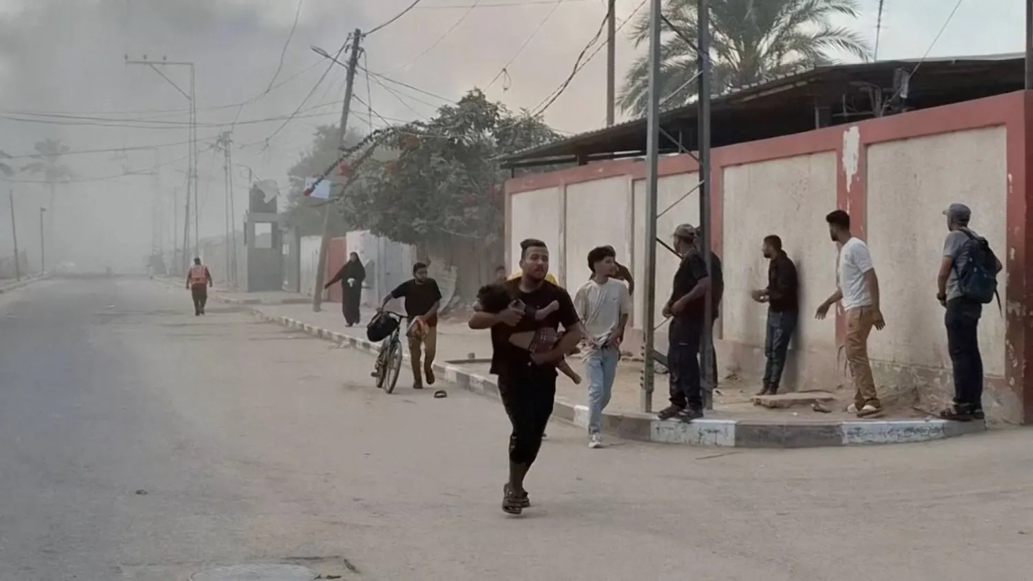 A man carrying a child runs as smoke rises following an Israeli airstrike, amid the ongoing conflict between Israel and Hamas, in Deir al-Balah, Gaza Strip, August 21, 2025, in this screengrab obtained from a video. Video obtained by Reuters/Handout via REUTERS