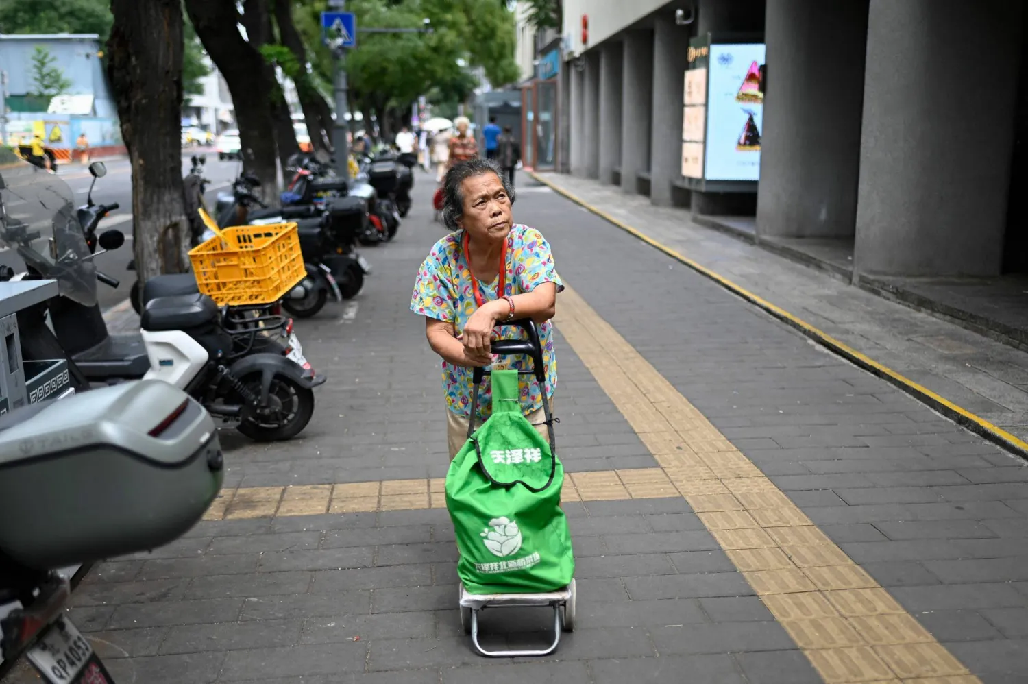 An elderly woman pushing her shopping trolley walks along a roaad in Beijing on August 18, 2025. (Photo by WANG Zhao / AFP)