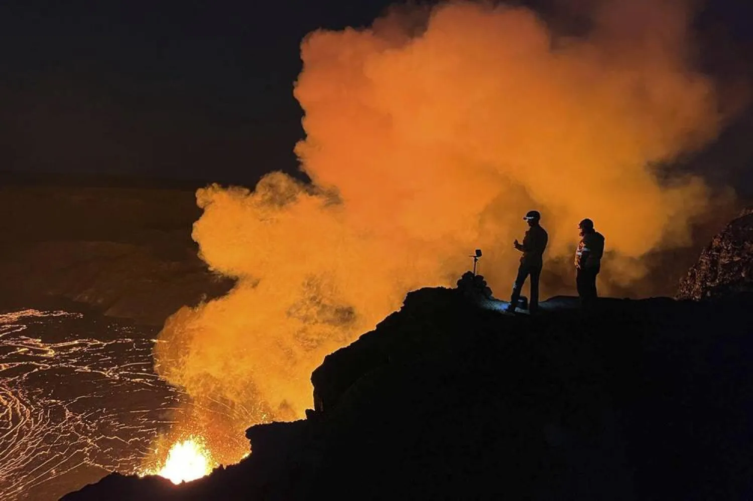 In this image provided the. the US Geological Survey (USGS), geologist deployed to the rim look over evening views of lava fountaining from Haleumaumau Crater at the summit of Kilauea volcano inside Hawaii Volcanoes National Park, Hawaii., Feb. 11, 2025. (J. Barnett/US Geological Survey via AP, File) 