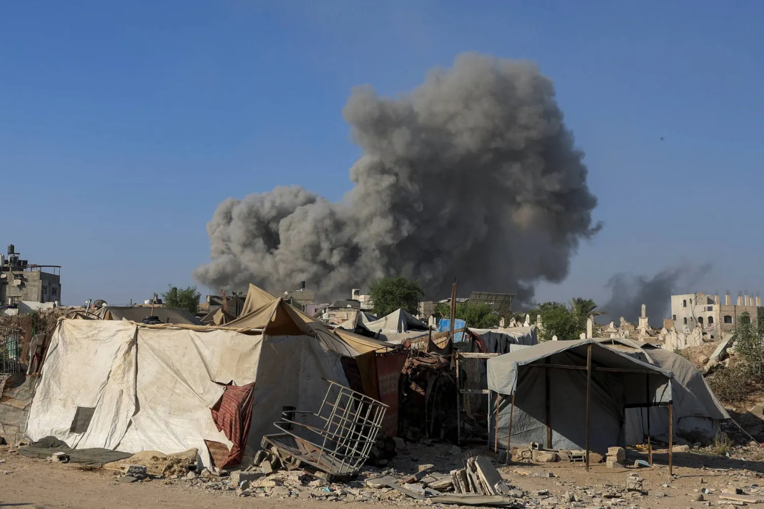دخان يتصاعد خلف مجموعة من الخيام جراء قصف إسرائيلي على مدينة غزة (رويترز) 