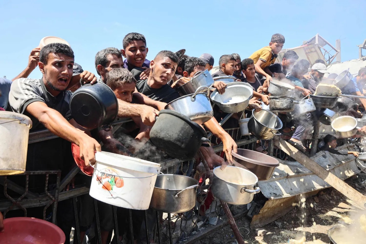 Palestinian men and boys extend their empty pots to receive cooked rice from charity kitchen in Gaza City on August 23, 2025. (Photo by Omar AL-QATTAA / AFP)