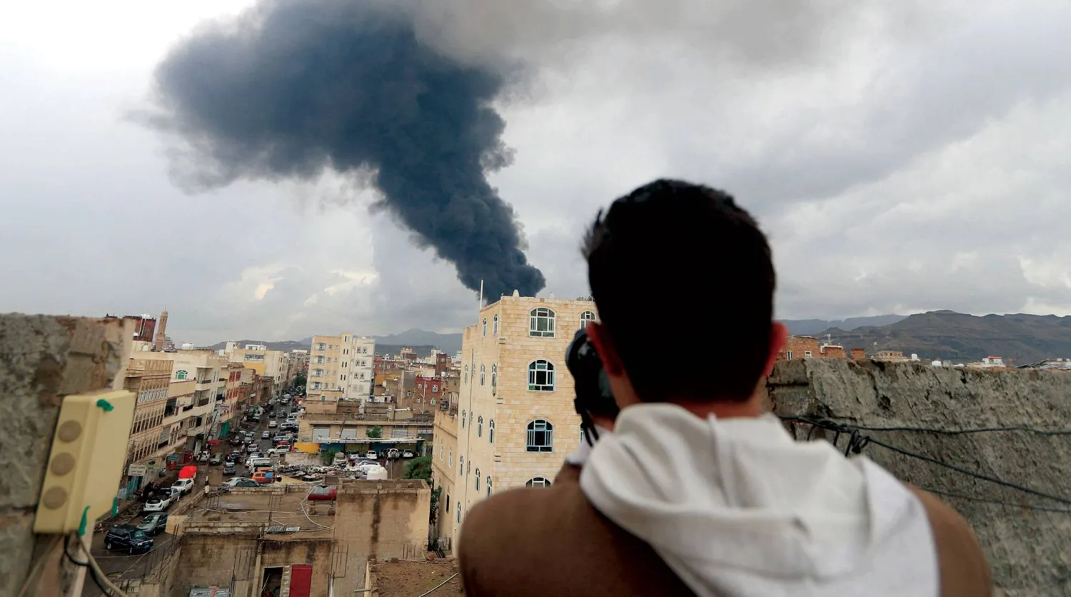 مصور صحافي يلتقط من سطح بناية في صنعاء صورة لموقع استهدفته ضربة إسرائيلية أمس (أ.ف.ب)