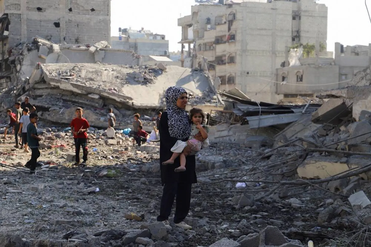 A Palestinian woman carries a child, as they inspect the site of an overnight Israeli strike on a house, in Gaza City, August 26, 2025. (Reuters) 