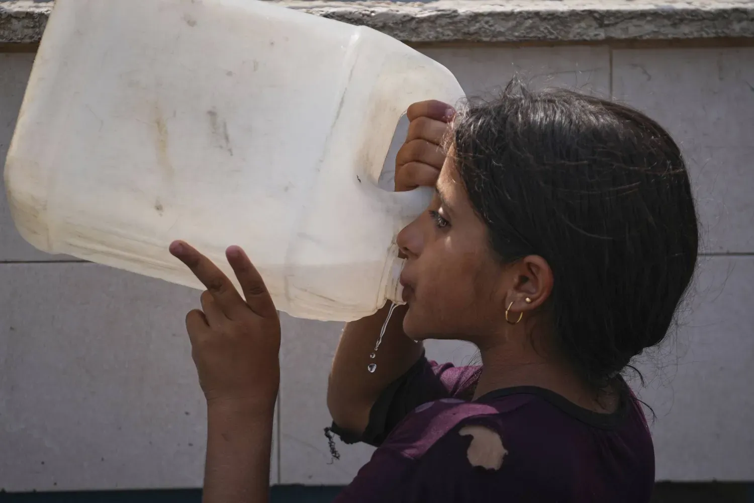 Filistinli bir kız, Gazze Şeridi'ndeki Deyr el-Belah'ta bulunan bir su istasyonunda plastik kovadan su içiyor (AP)