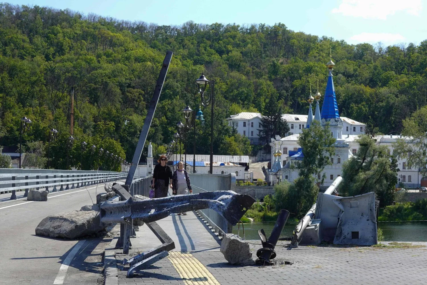 أشخاص يسيرون عبر الجسر في سفياتوغورسك بمنطقة دونيتسك في 27 أغسطس2025 بعد أن تضرر من جراء غارة جوية حديثة خلال الغزو الروسي لأوكرانيا (أ.ف.ب)