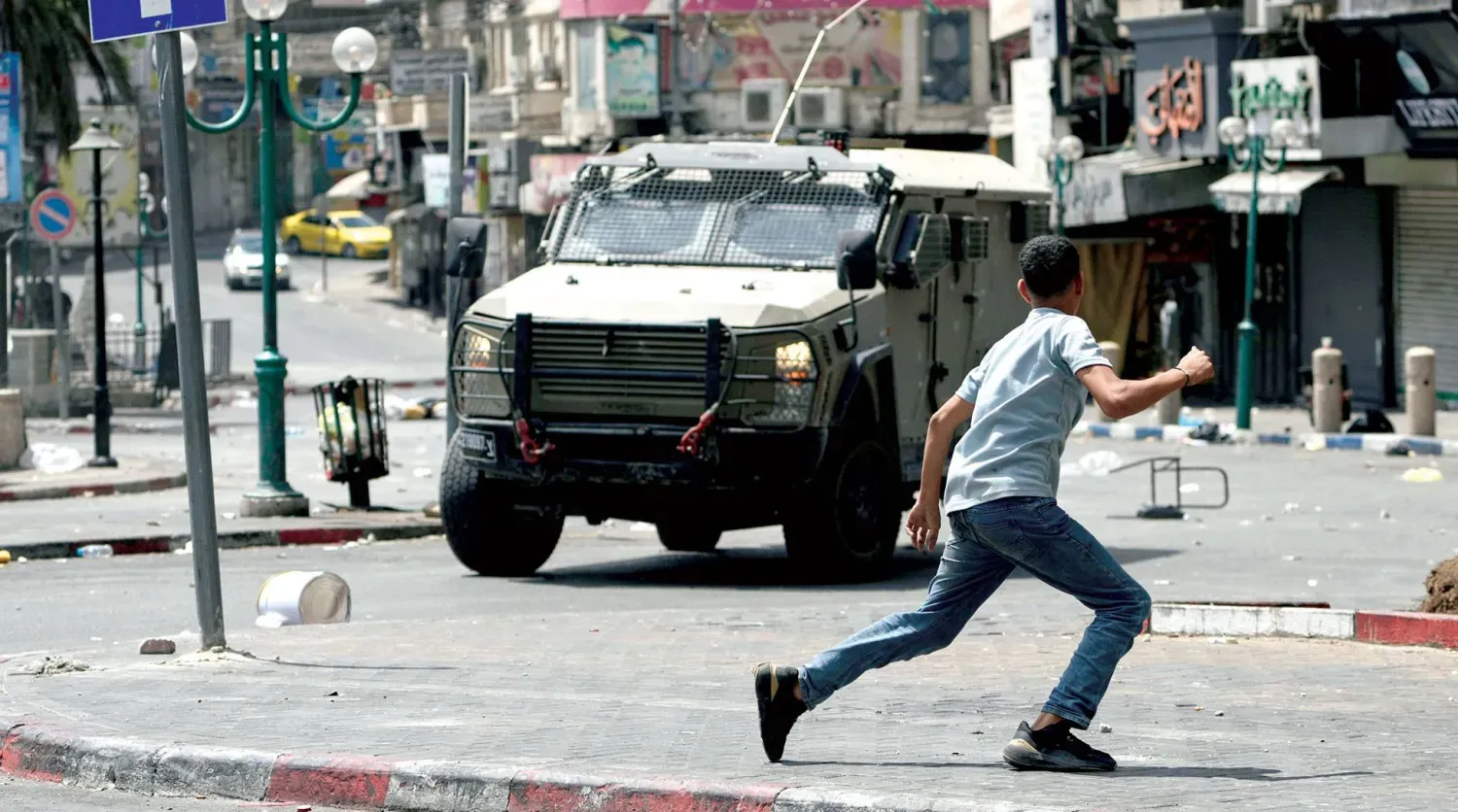 Filistinli genç, İsrail ordusunun dün Nablus şehrine saldırmasının ardından askeri bir aracın önünde koşuyor (AP)