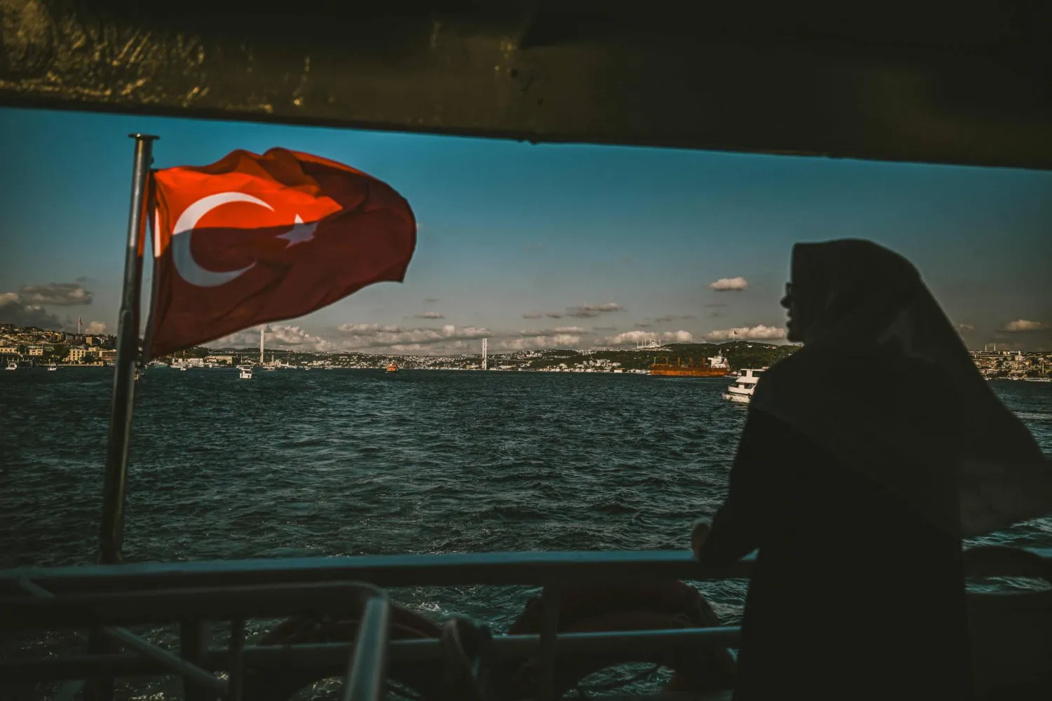A woman looks out from a ferry as the 15 July Martyrs Bridge (known as Bosphorus bridge) is seen in the backround in Istanbul on August 18, 2025. (Photo by Ozan KOSE / AFP)