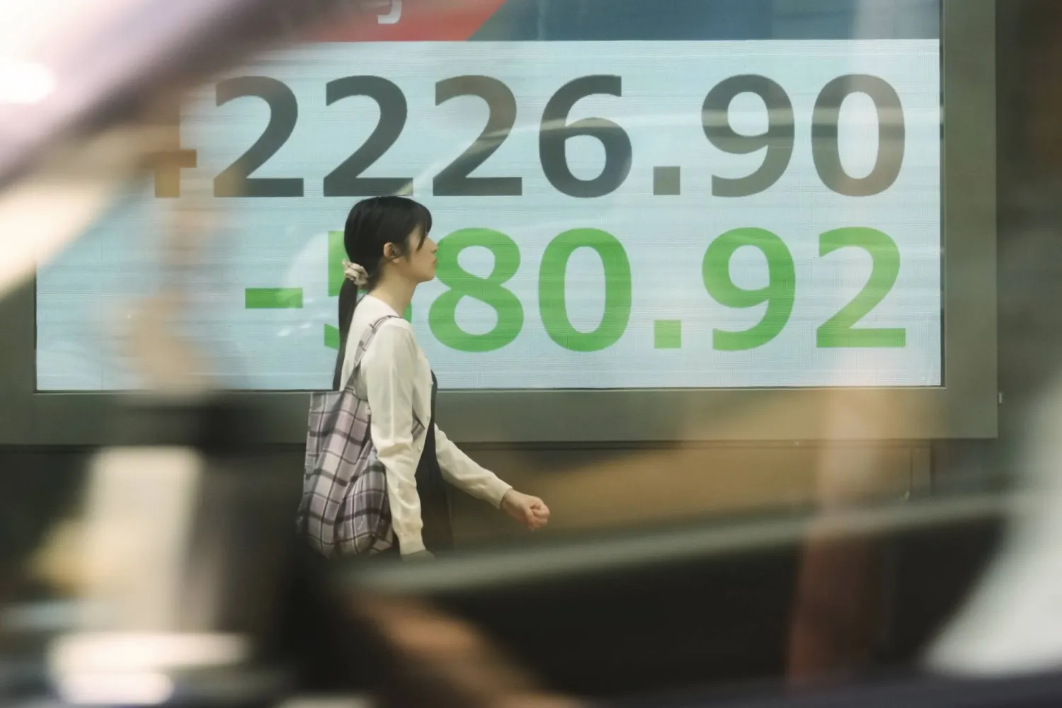 امرأة تمر أمام لوحة تعرض حركة الأسهم وسط العاصمة اليابانية طوكيو (أ.ب)