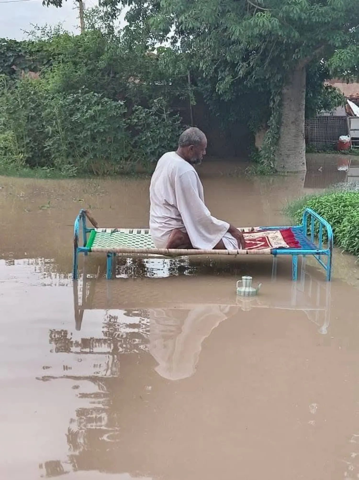 مواطن يؤدي الصلاة على سرير وسط المياه في الخرطوم (فيسبوك)