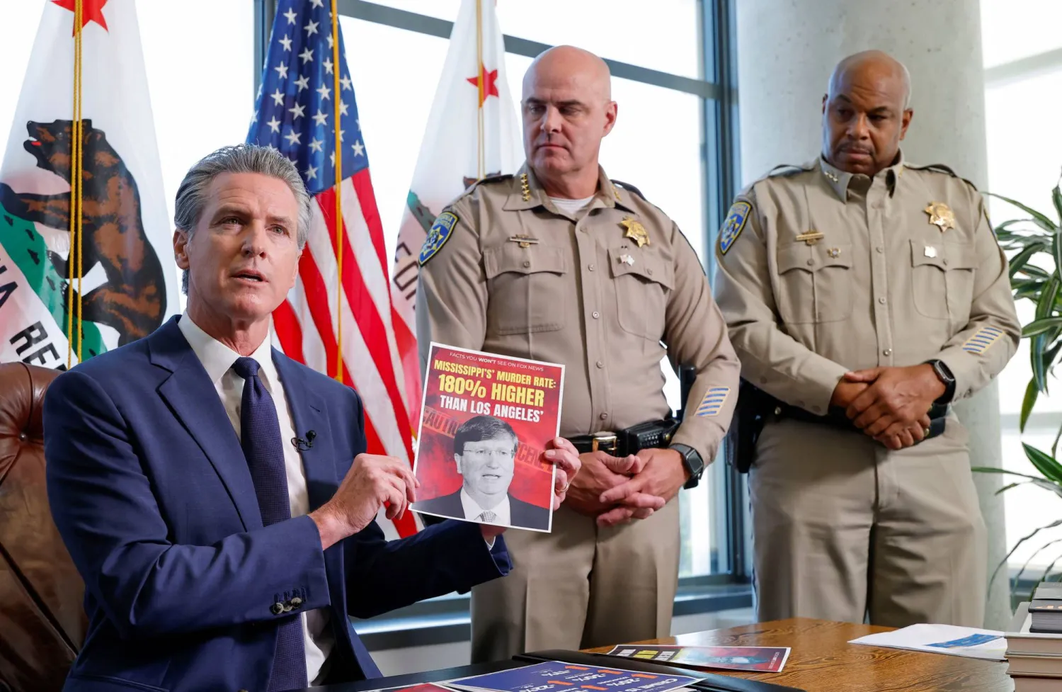 حاكم ولاية كاليفورنيا غافين نيوسوم يحمل ملصقاً عليه صورة حاكم ولاية ميسيسيبي تيت ريفز يقارن معدل الجريمة في كاليفورنيا بمعدل ميسيسيبي أثناء إعلانه عن الجهود المبذولة للحد من الجريمة خلال مؤتمر صحافي في مكتبه في ساكرامنتو... ولاية كاليفورنيا الأميركية 28 أغسطس 2025 (رويترز)