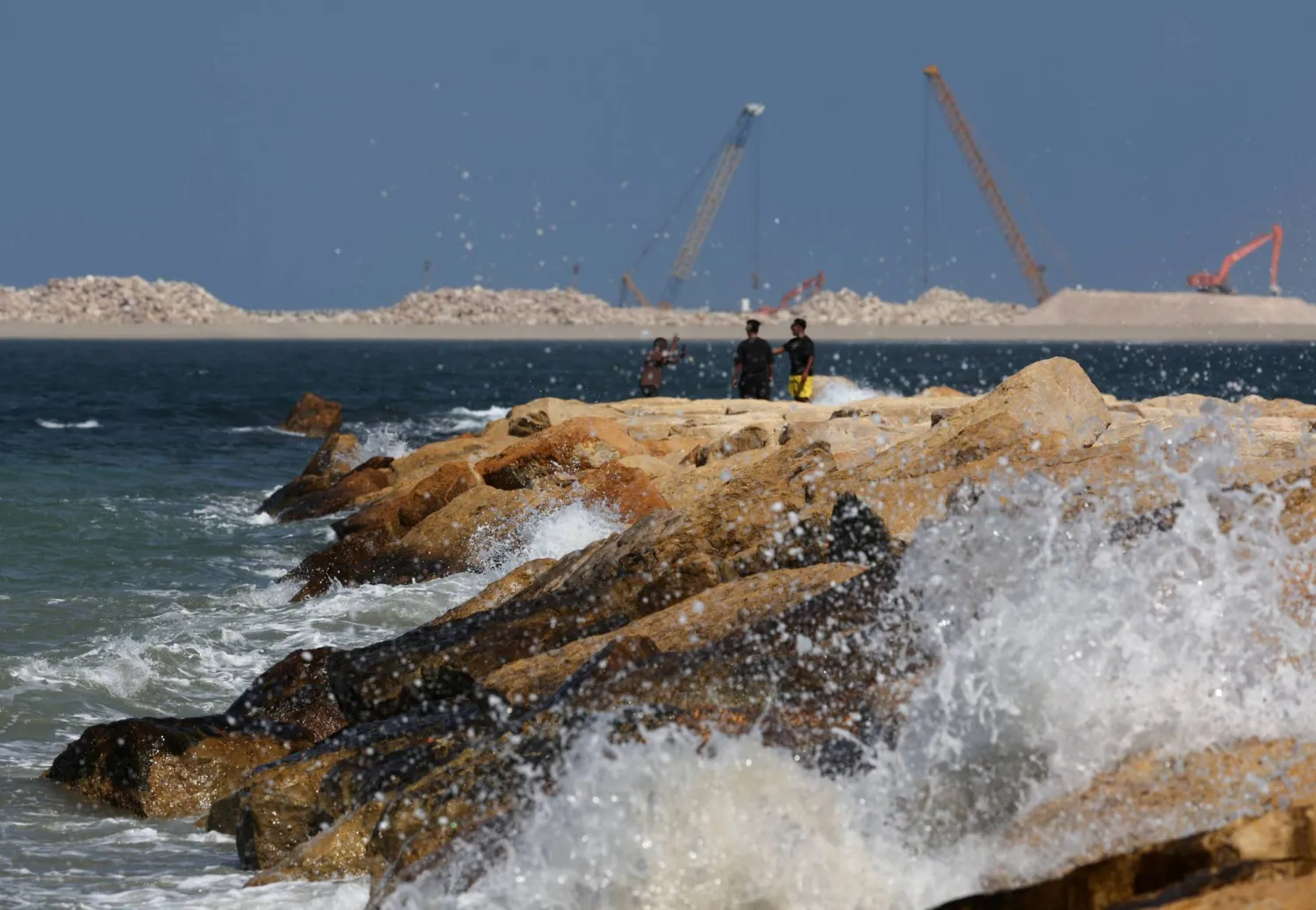 Waves crash on the rocks while people gather on the shore near a construction site, as a new barrier is built to protect Alexandria's shoreline, on the Mediterranean coast, in Alexandria, Egypt, August 21, 2025. REUTERS/Amr Abdallah Dalsh