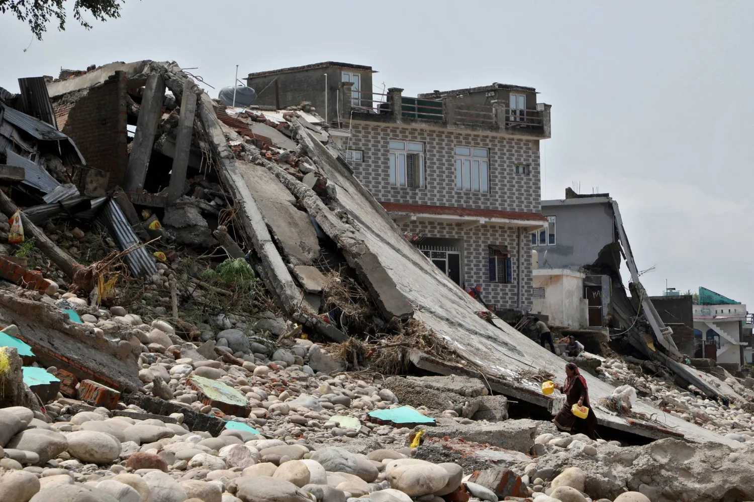 امرأة تحمل عبوات بلاستيكية عثرت عليها في ركام منزلها الذي ضربته السيول في جامو (رويترز)