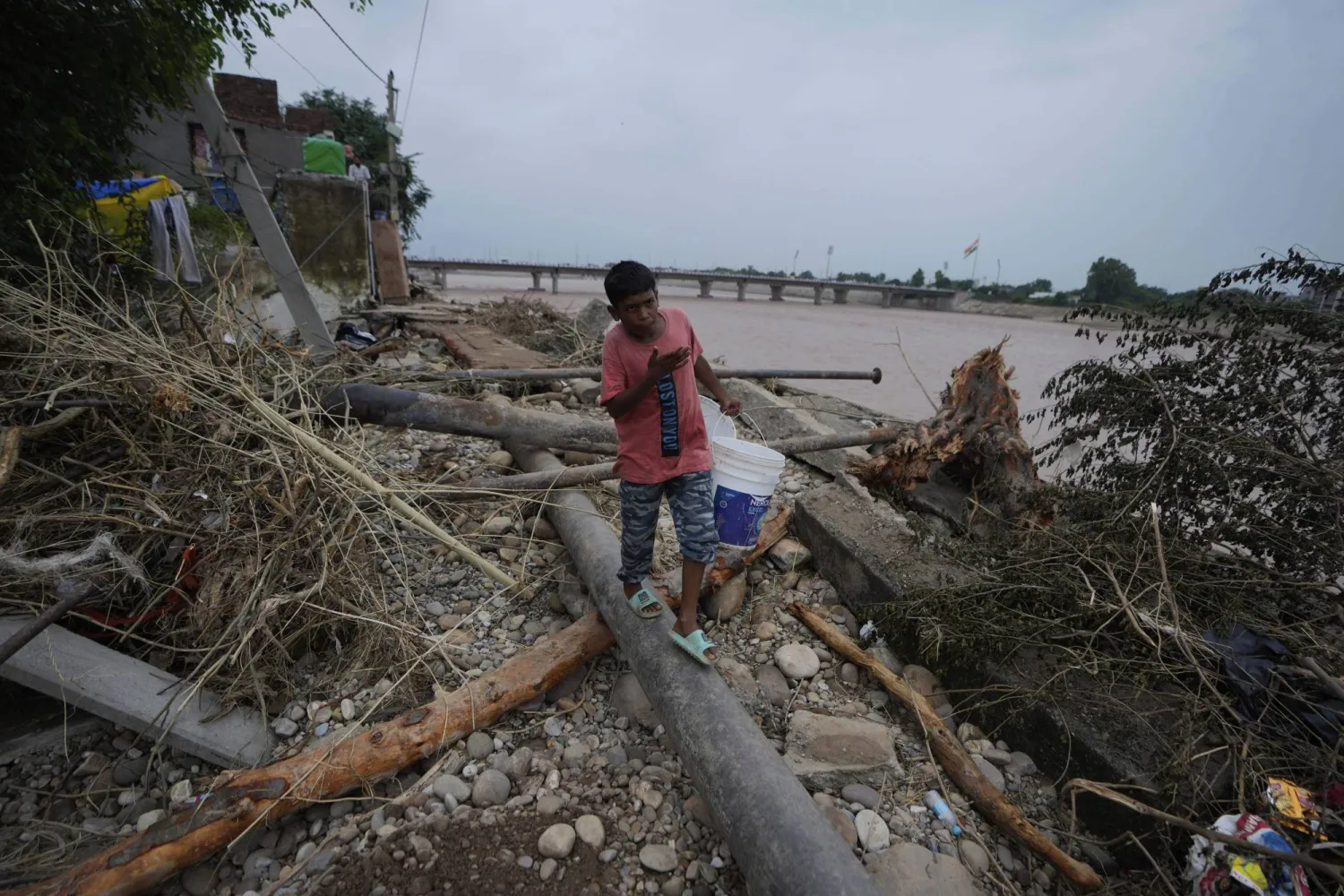 An Indian boy carries a bucket in search of drinking water near the flood-hit banks of the Tawi River in Jammu, India, Saturday, Aug. 30, 2025.(AP Photo/Channi Anand)