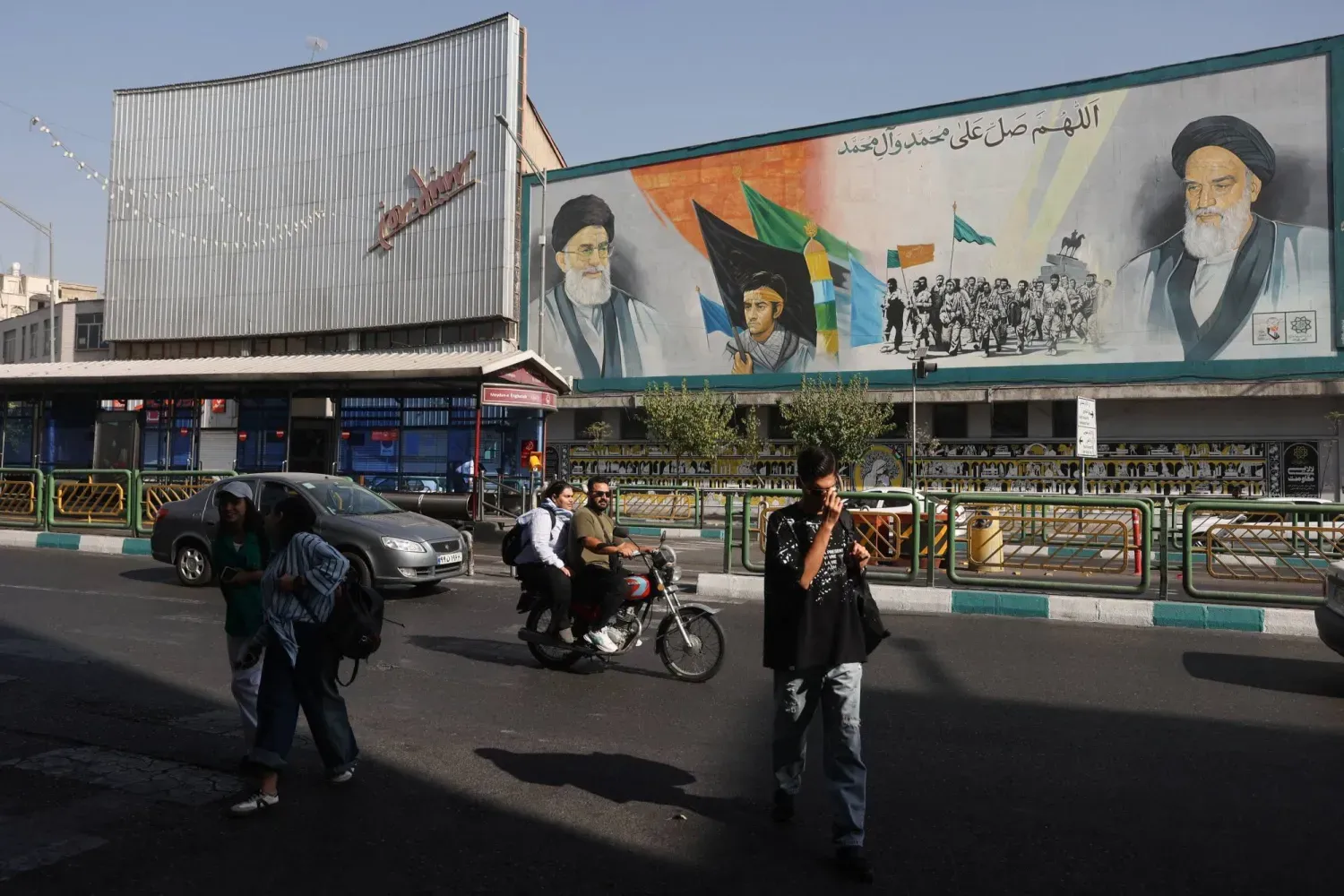 Tahran'da bir caddede İran Dini Lideri Ali Hamaney'in resminin bulunduğu bir duvarın önünden geçen insanlar, 29 Ağustos 2025 (Reuters)