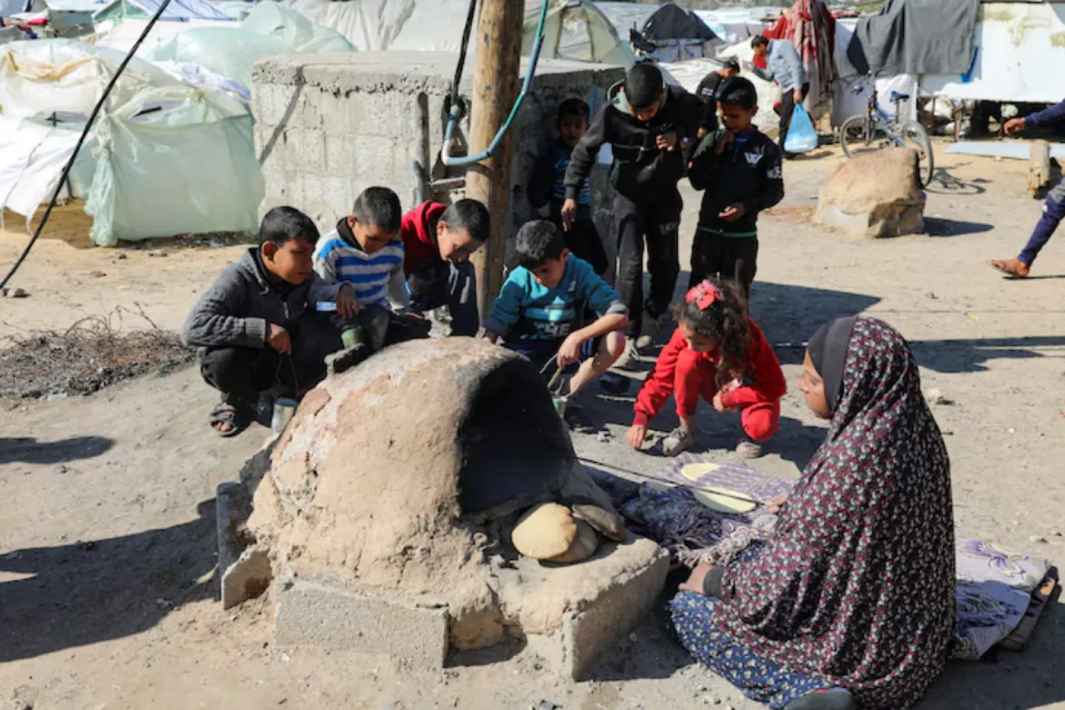 A Palestinian woman bakes bread as children sit next to her, while Gaza residents face crisis levels of hunger and soaring malnutrition, in Khan Younis in the southern Gaza Strip January 24, 2024. REUTERS/Arafat Barbakh/File Photo 
