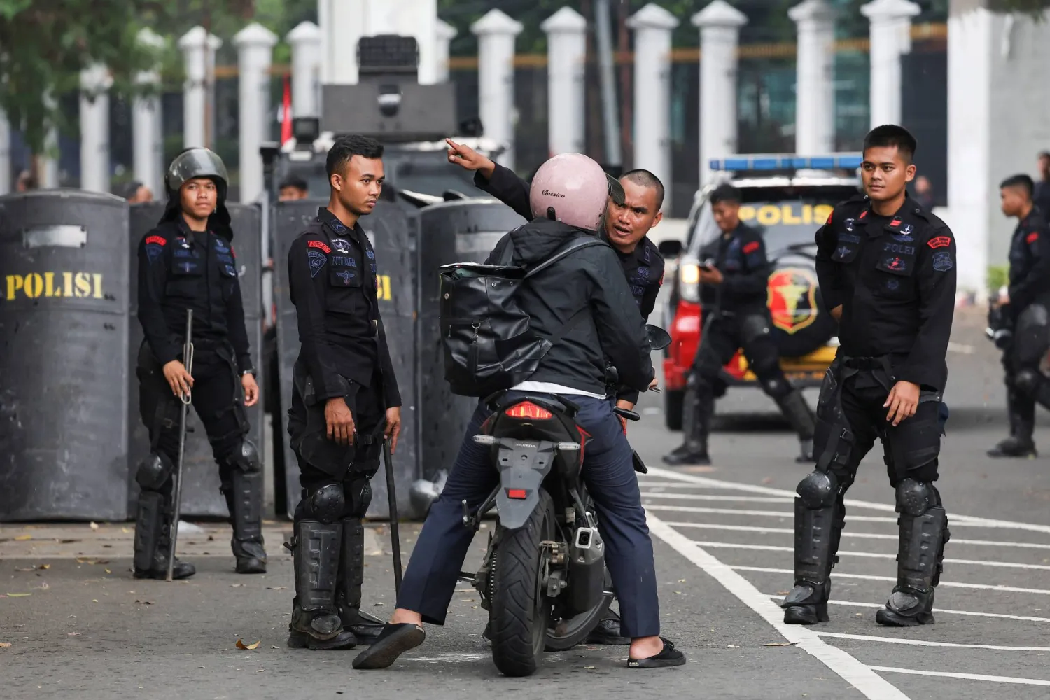 شرطة مكافحة الشغب تفحص سائق دراجة بخارية خارج مبنى البرلمان الإندونيسي (رويترز)