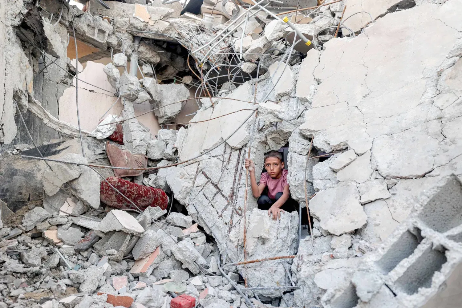 Filistinli bir çocuk, Gazze Şeridi'nin merkezindeki Nuseyrat mülteci kampında İsrail bombardımanında yıkılan bir binanın enkazından dışarı bakıyor (AFP)