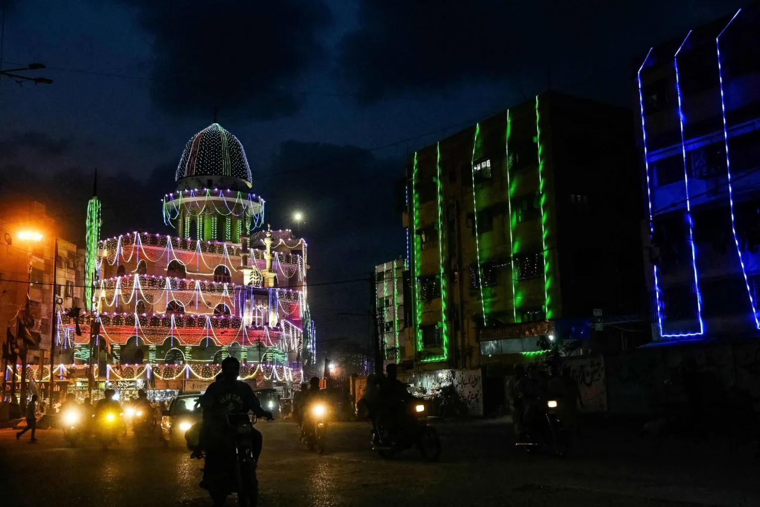 Commuters ride past a mosque illuminated ahead of Eid-e-Milad-un-Nabi, which commemorates the birth anniversary of Prophet Mohammed in Karachi on August 30, 2025. (Photo by Rizwan TABASSUM / AFP)