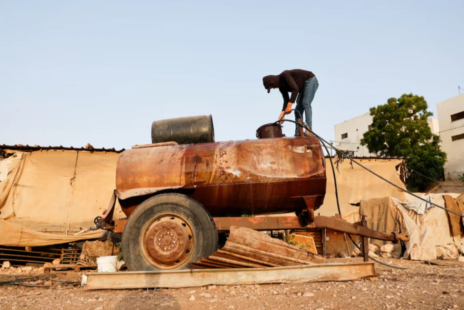 A Palestinian man fills a water tank in Bardala, in Jordan Valley, in the Israeli-occupied West Bank August 13, 2025. REUTERS/Ammar Awad 