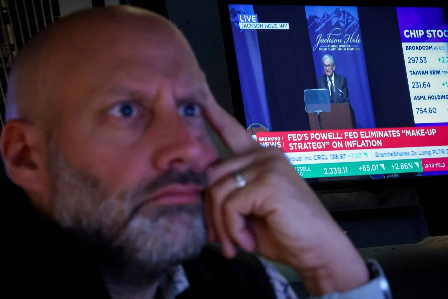 متداول ببورصة نيويورك يراقب تطور أسعار الأسهم وخلفه شاشة تُظهر رئيس «الاحتياطي الفيدرالي» جيروم باول وهو يتحدث في أغسطس (رويترز)