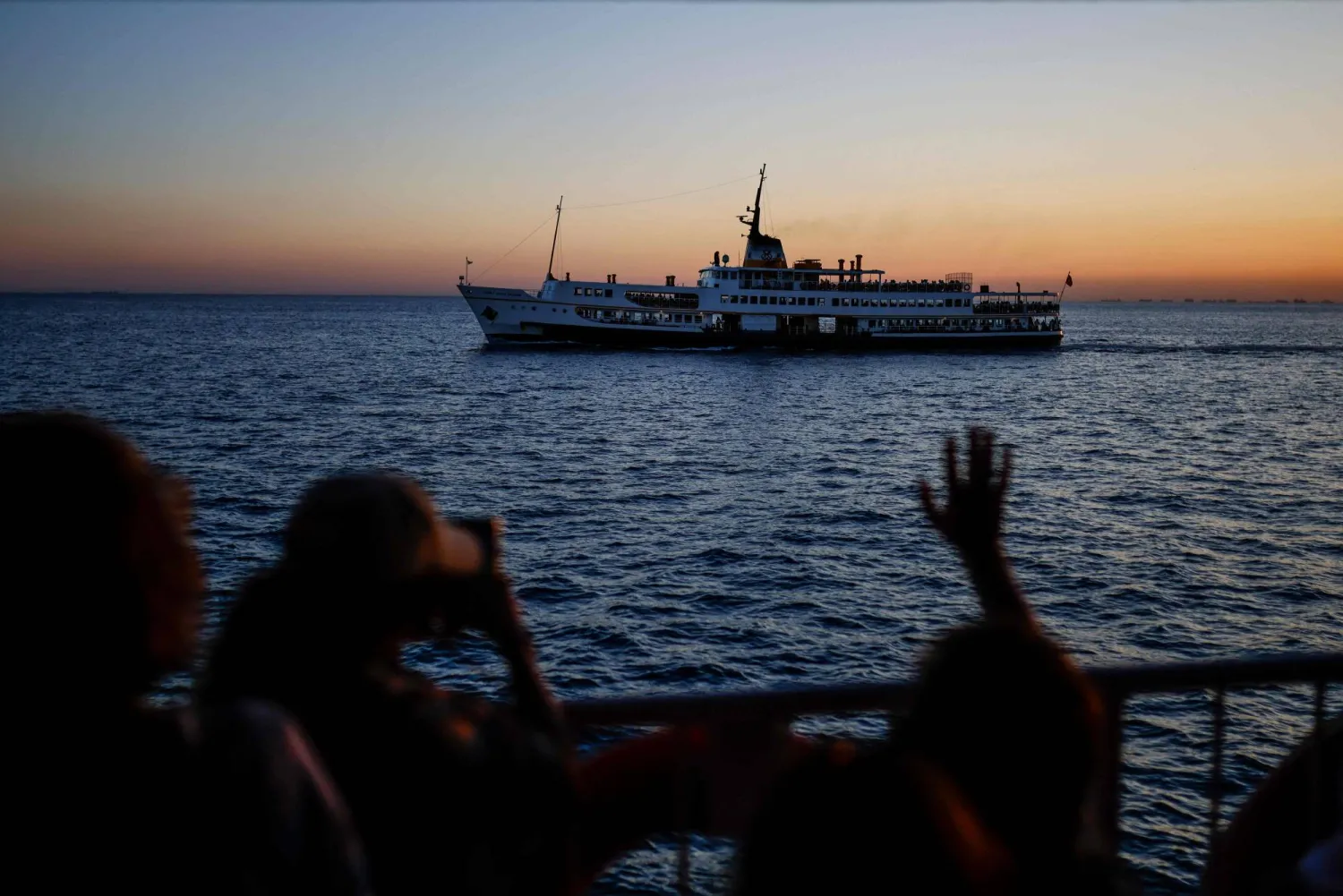 Passengers wave at anothger boat as they sail aboard the Pasabahce ferryboat to Princes islands in Istanbul, on August 21, 2025. (Photo by KEMAL ASLAN / AFP)