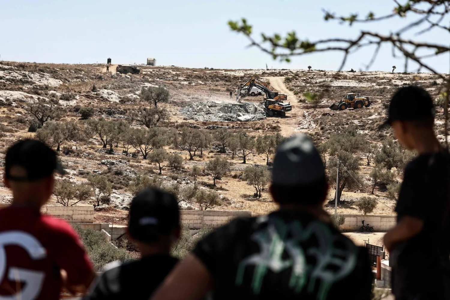 شباب فلسطينيون يشاهدون آليات تابعة لجيش الاحتلال الإسرائيلي تهدم منازل فلسطينيين في إحدى قرى رام الله بالضفة الغربية المحتلة قبل يومين (أ.ف.ب)