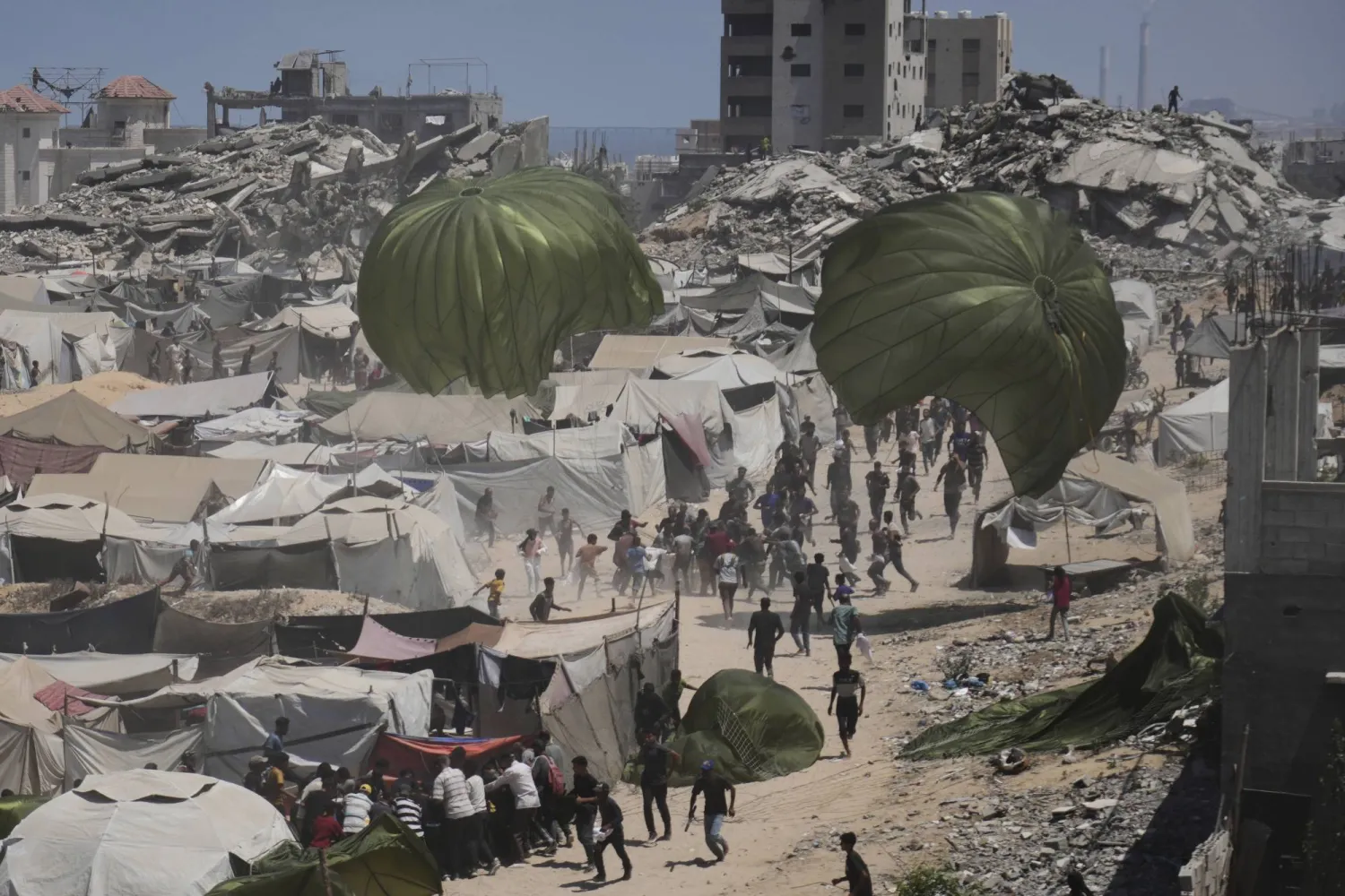 فلسطينيون يسارعون إلى تسلم المساعدات الإنسانية التي ألقيت بالمظلات على مدينة غزة شمال القطاع (أ.ب)