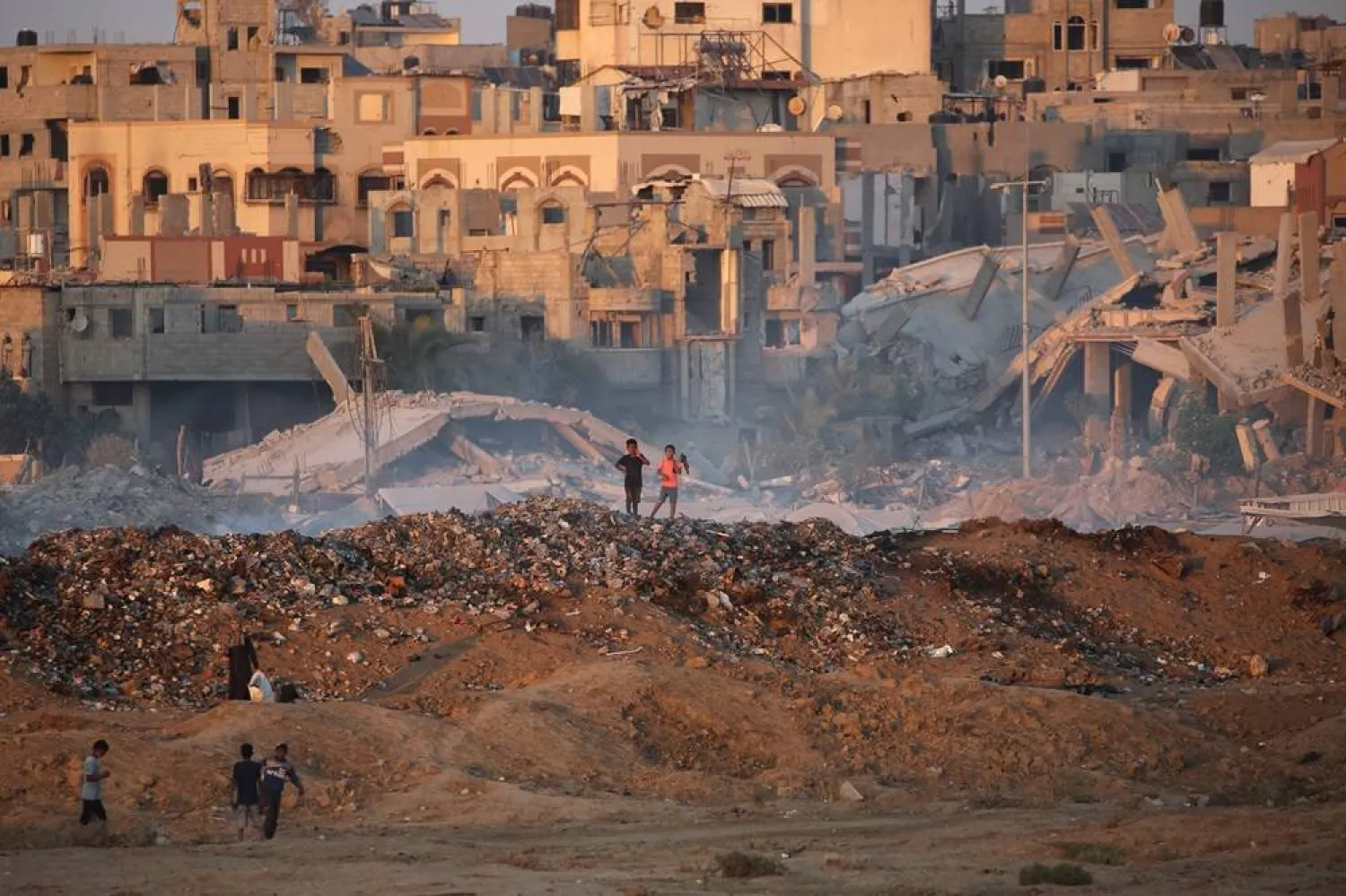 Palestinian children walk over a mound of dirt and trash at the Bureij camp for displaced Palestinians in the central Gaza Strip on September 3, 2025. (AFP)