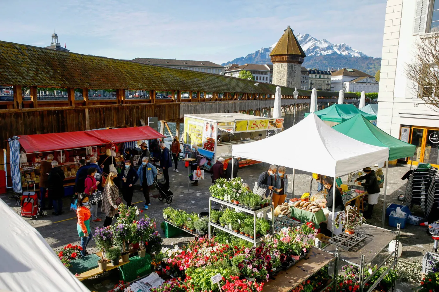 جبل بيلاتوس المغطى بالثلوج وجسر كابيل بروكه التاريخي خلف سوق أسبوعي في لوزيرن (رويترز)