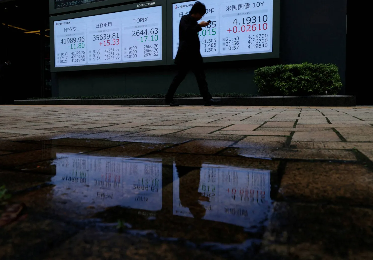 رجل يمر أمام لوحة أسعار أسهم تُظهر مؤشر داو جونز ومتوسط ​​أسهم «نيكي» وعائد سندات الحكومة اليابانية والأميركية في طوكيو (رويترز)