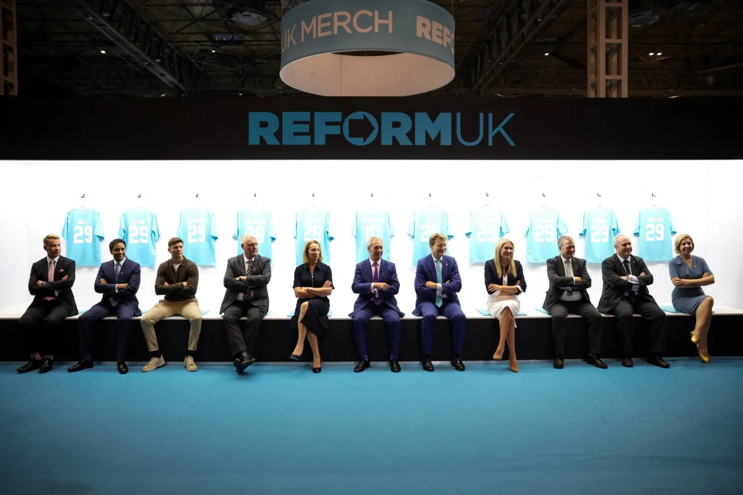 يجلس زعيم حزب «الإصلاح» البريطاني نايجل فاراج وأعضاء الحزب بجوار قمصانهم الرياضية خلال اليوم الثاني من مؤتمر الحزب في برمنغهام (رويترز)