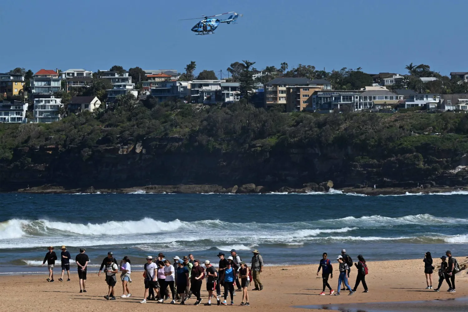 Visitors avoid the water while a helicopter scans the ocean as northern Sydney beaches are closed following a shark attack at Long Reef Beach on September 6, 2025. (Photo by Saeed KHAN / AFP)