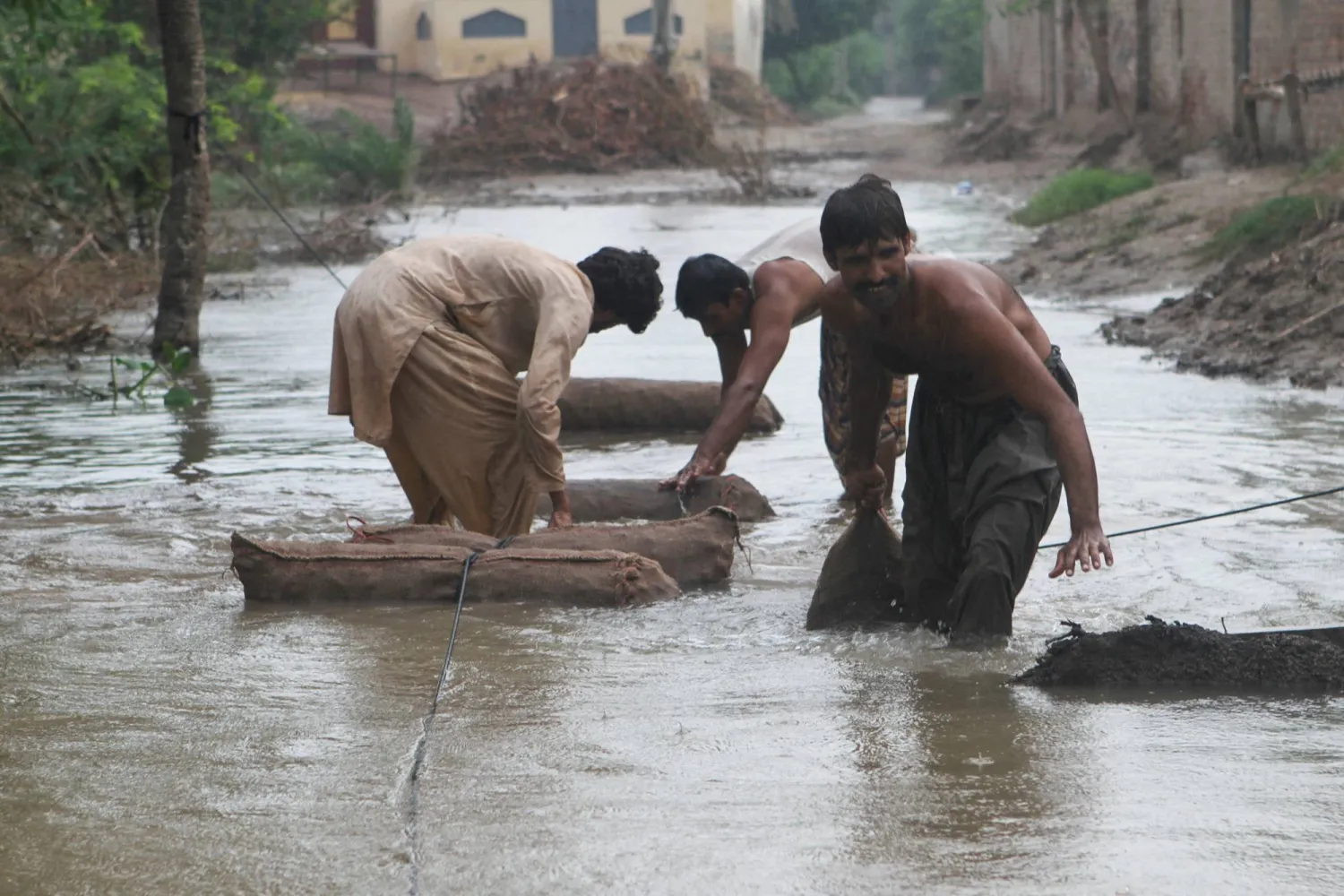 Farmers move sacks of taro root vegetable through a flooded street amid rain, following monsoon rains and rising water levels of the Chenab River, in Qasim Bela village on the outskirts of Multan, Punjab province, Pakistan September 7, 2025. REUTERS/Quratulain Asim