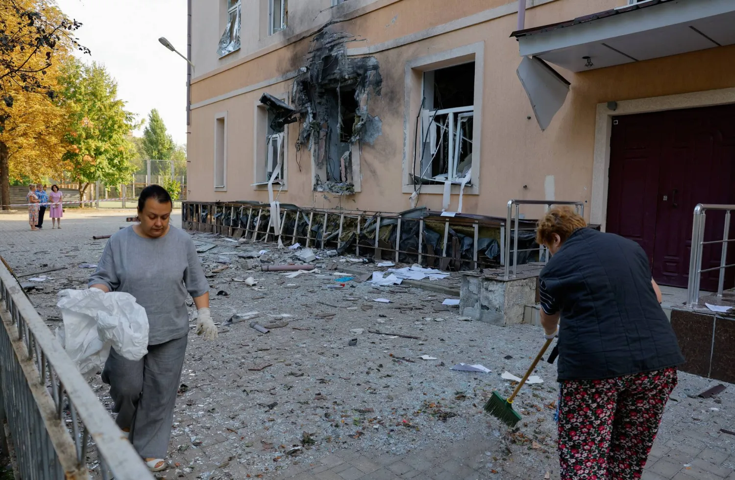 نساء يُزِلن الحطام خارج مبنى مدرسة متضرر في دونيتسك (رويترز)