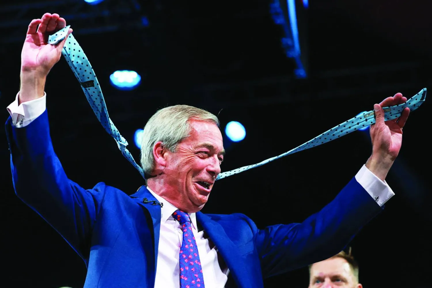 زعيم حزب «ريفورم» نايجل فاراج يحمل ربطة عنق أُلقيت من الجمهور على المسرح خلال مؤتمر الحزب في برمنغهام (رويترز)