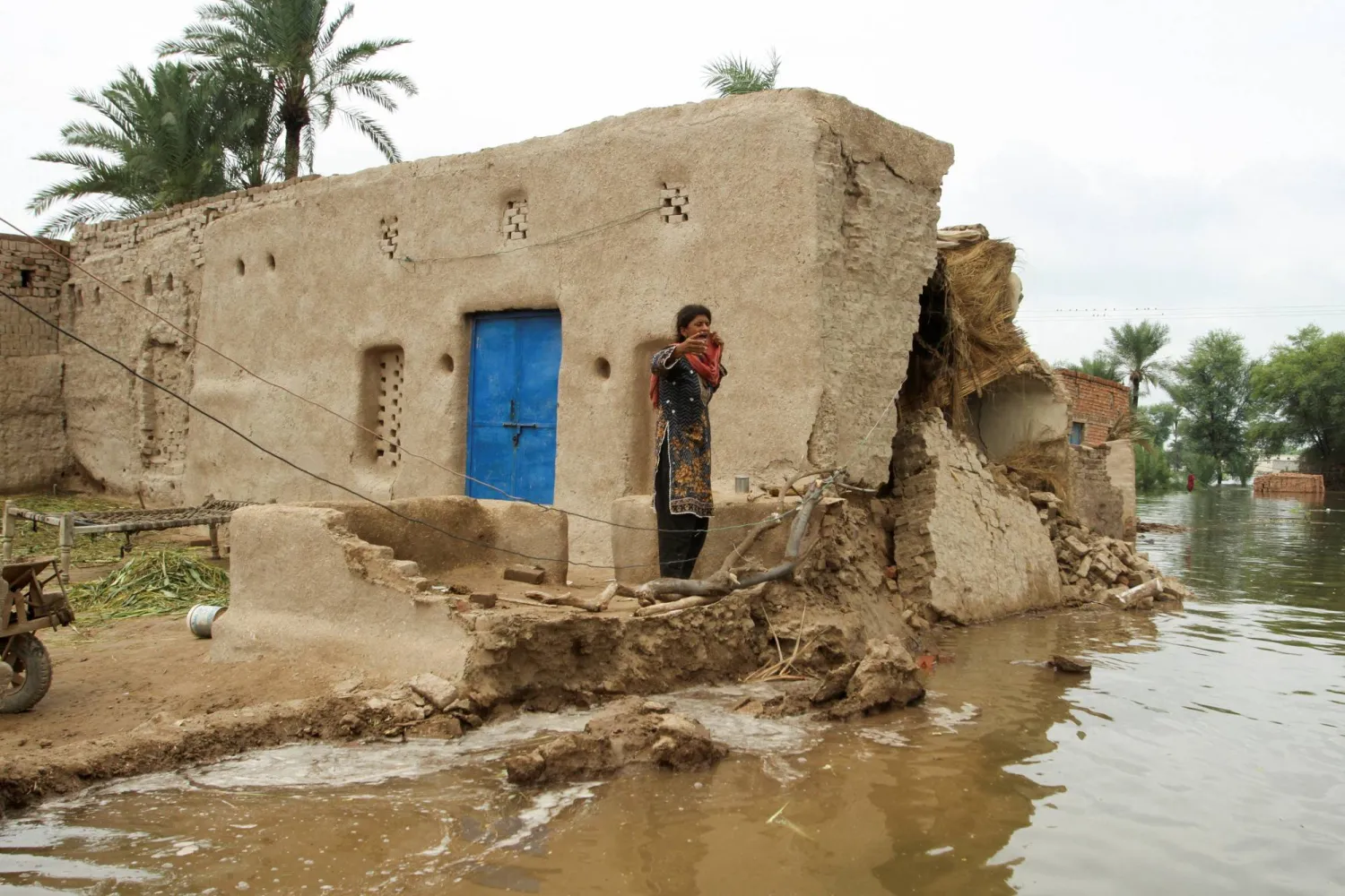 يقف أحد السكان عند منزل متضرر جزئياً وسط منطقة غمرتها المياه في أعقاب الأمطار الموسمية وارتفاع منسوب مياه نهر تشيناب في جلالبور بيروالا بإقليم البنجاب (رويترز)