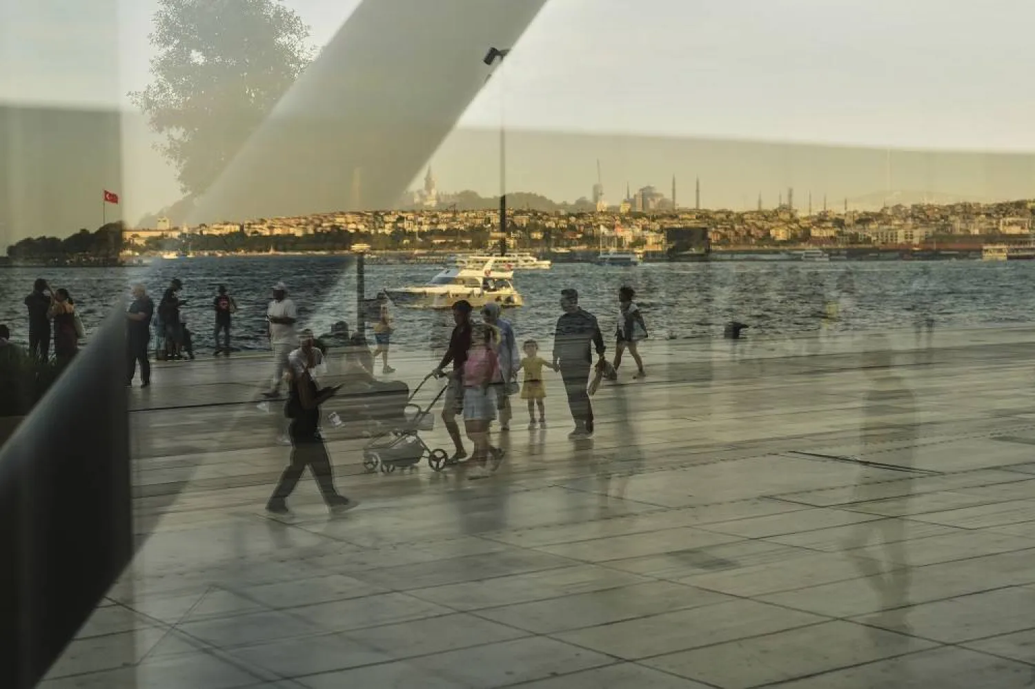 Passersby, seen through a security glass, walk along the Galataport sea promenade next to the Bosphorus, in Istanbul, Türkiye, Thursday, Sept. 11, 2025. (AP) 