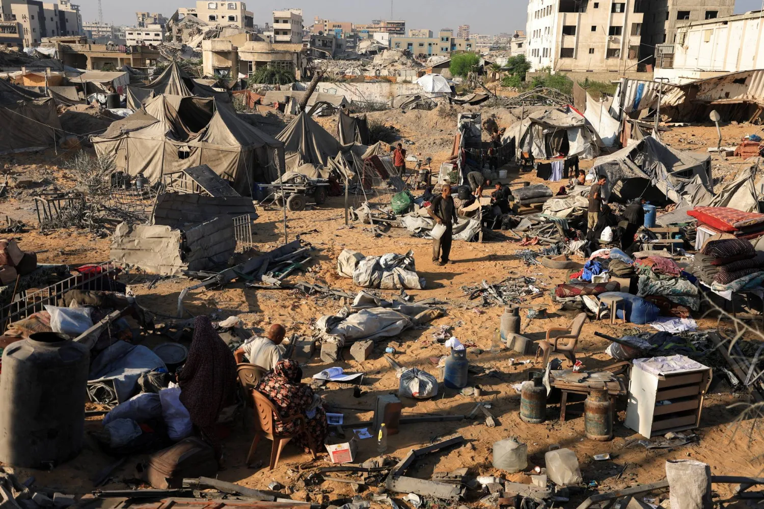 فلسطينيون يتفقدون مخيماً كان يؤوي النازحين بعد أن تضرر في غارة جوية إسرائيلية ليلية على مبنى سكني في مدينة غزة (رويترز)