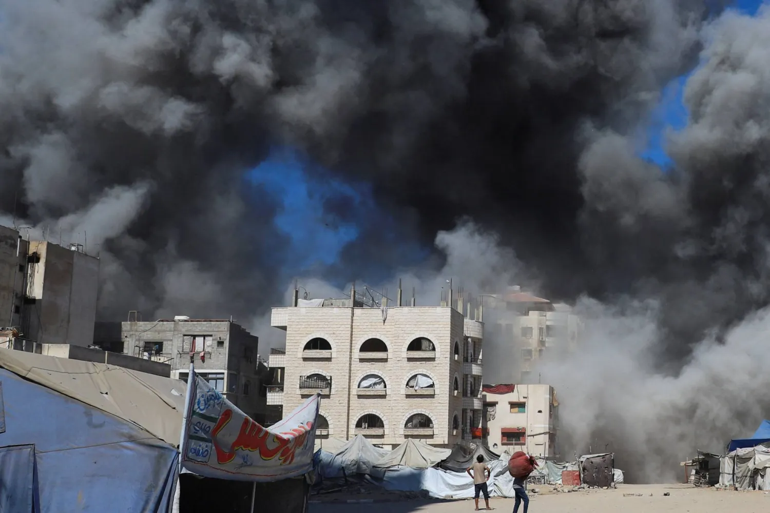 فلسطينيون ينظرون إلى الدخان المتصاعد من مبنى سكني كان يؤوي فلسطينيين نازحين بعد أن ضربته غارة جوية إسرائيلية في مدينة غزة (رويترز)