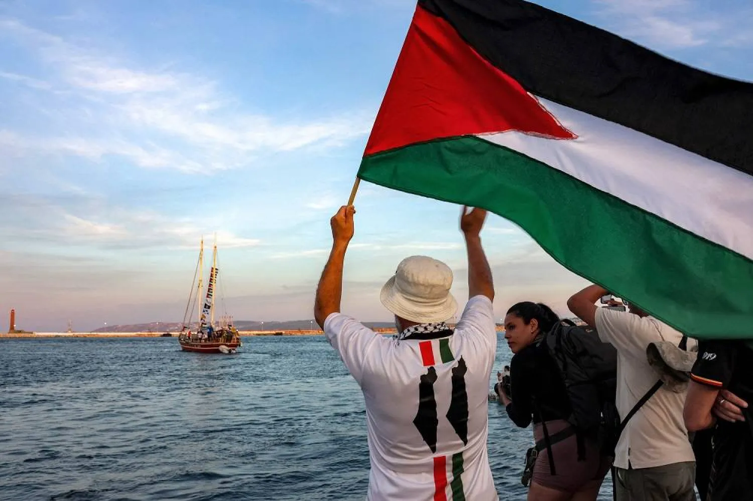 A man waves a Palestinian flags to other activists and human rights defenders riding aboard a vessel departing from Tunisia's northern port of Bizerte on September 14, 2025 to join the last boats taking part in the Global Sumud Flotilla, bound for the Gaza Strip to break Israel's blockade on the Palestinian territory. (AFP)