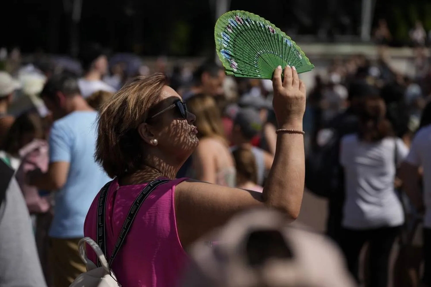 A tourist uses a fan to shade her face from the sun while waiting to watch the Changing of the Guard ceremony outside Buckingham Palace, during hot weather in London, July 18, 2022. (AP)
