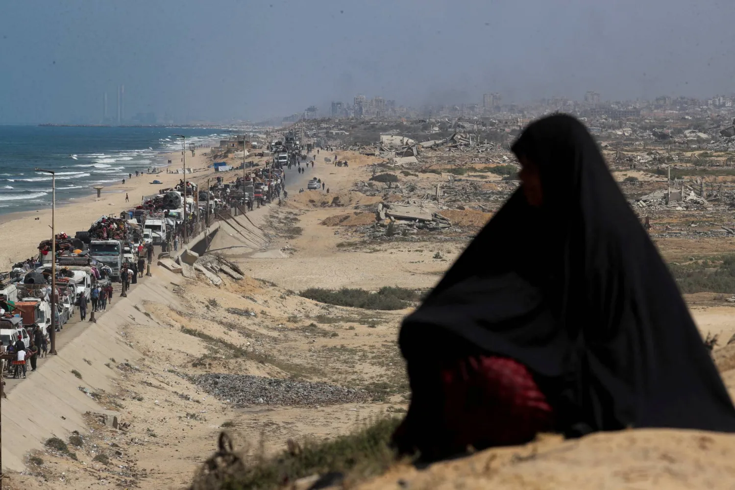 امرأة تراقب الفلسطينيين النازحين الفارين من شمال غزة بسبب الحرب الإسرائيلية وهم يتحركون جنوباً بعد أن أمرت القوات الإسرائيلية سكان مدينة غزة بالإخلاء إلى الجنوب في وسط قطاع غزة (رويترز)