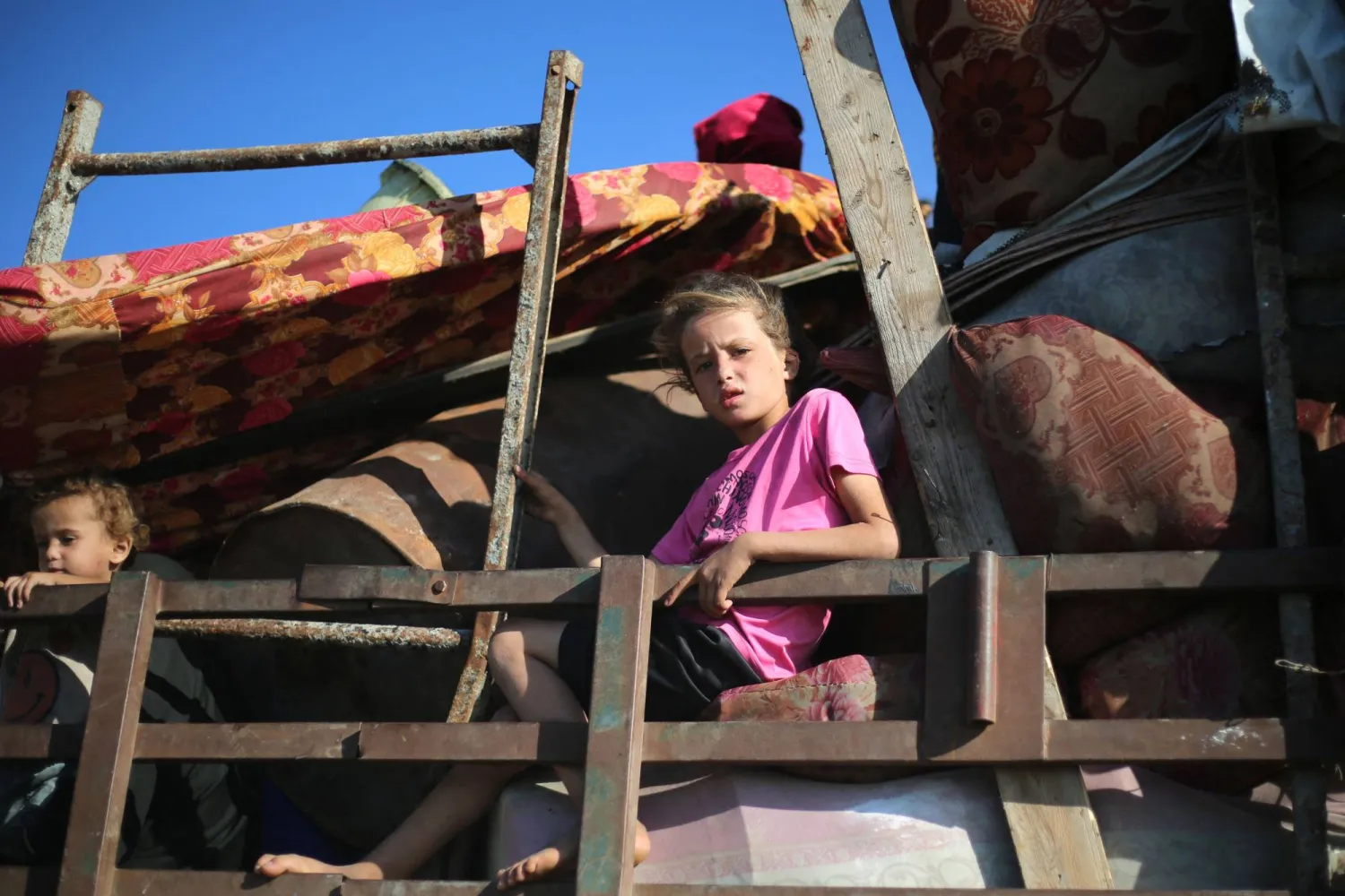 طفلة فلسطينية نازحة أعلى سطح عربة على طريق بمخيم النصيرات (أ.ف.ب)