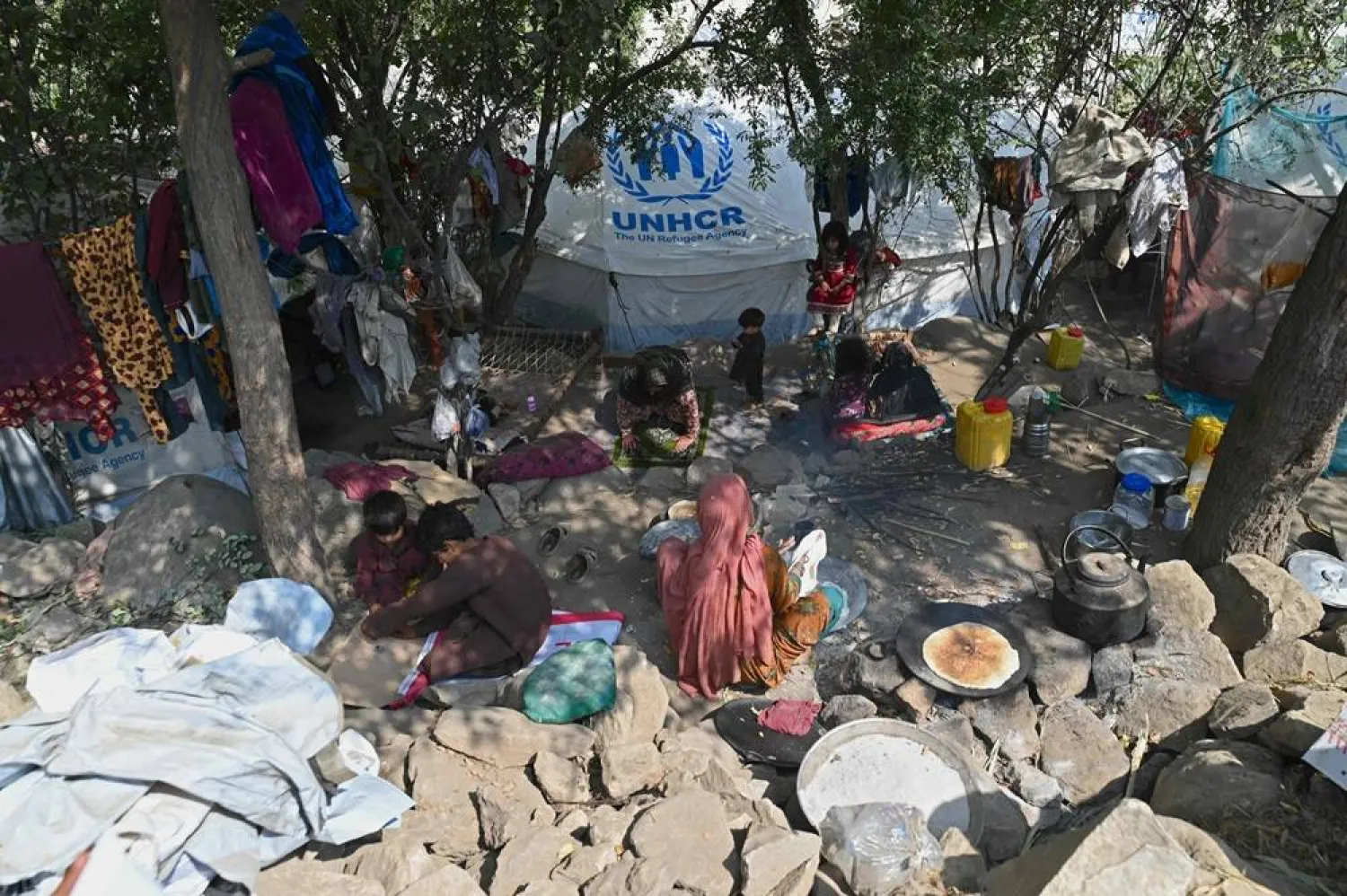 An Afghan woman cooks bread as she sits near a makeshift tent with a logo of UNHCR (United Nations High Commissioner for Refugees), set up outside her damaged house in the aftermath of an earthquake at Mazar Dara village in Nurgal district, Kunar province on September 14, 2025. (AFP) 