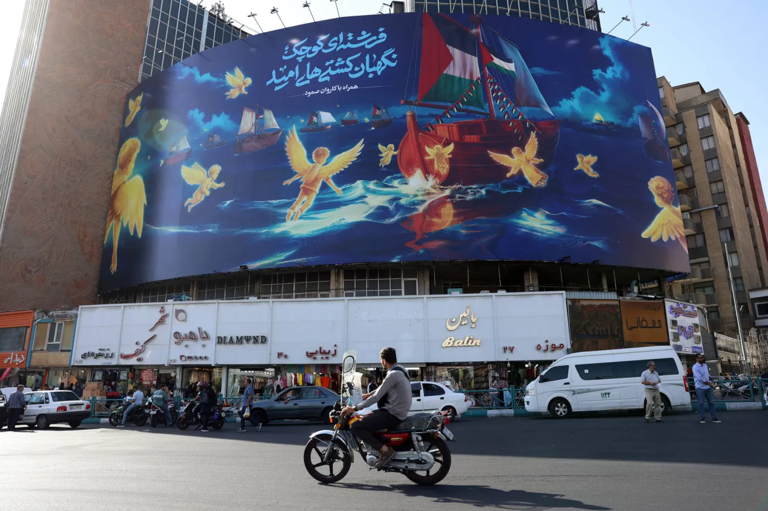 Iranians drive past next to a pro-Palestine billboard carrying Palestine flags and a sentence reading in Persian, 'Little angel will guard the hope ships', at the Valiasr square in Tehran, Iran, 18 September 2025.  EPA/ABEDIN TAHERKENAREH