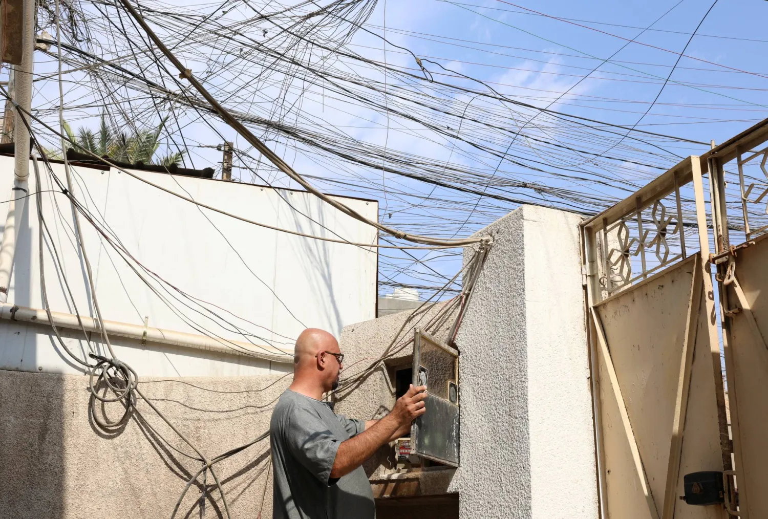 Resident Omar Hameed Abed, 47, checks the electricity switchboard in his home, with a network of generator wires visible above, in Baghdad, Iraq, September 18, 2025. REUTERS/Ahmed Saad