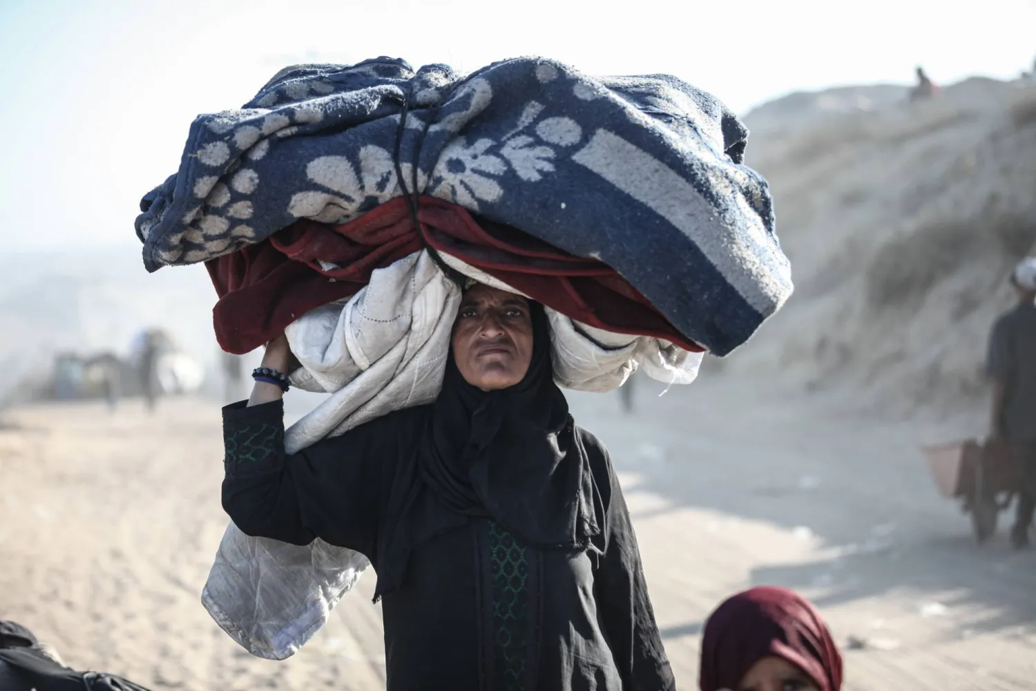 فلسطينية تحمل أمتعة على رأسها خلال النزوح سيراً على الأقدام في اتجاه جنوب قطاع غزة (د.ب.أ)